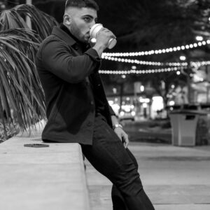 A monochrome photo of a man drinking coffee outdoors at night, capturing a relaxed urban vibe.