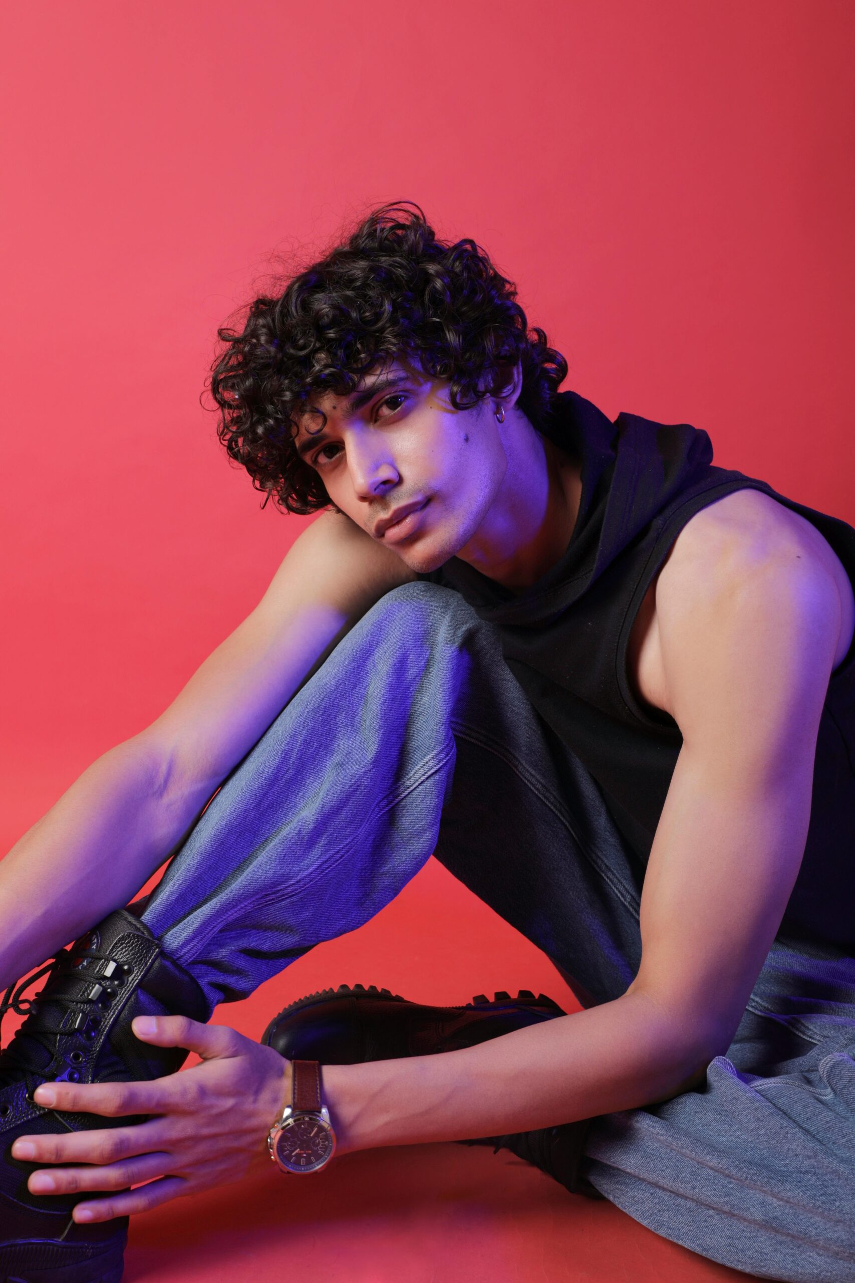 A fashionable man in casual attire posing confidently against a bold red background.