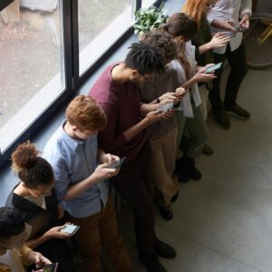 A group of diverse office workers standing by a window using smartphones, capturing modern workplace connectivity.
