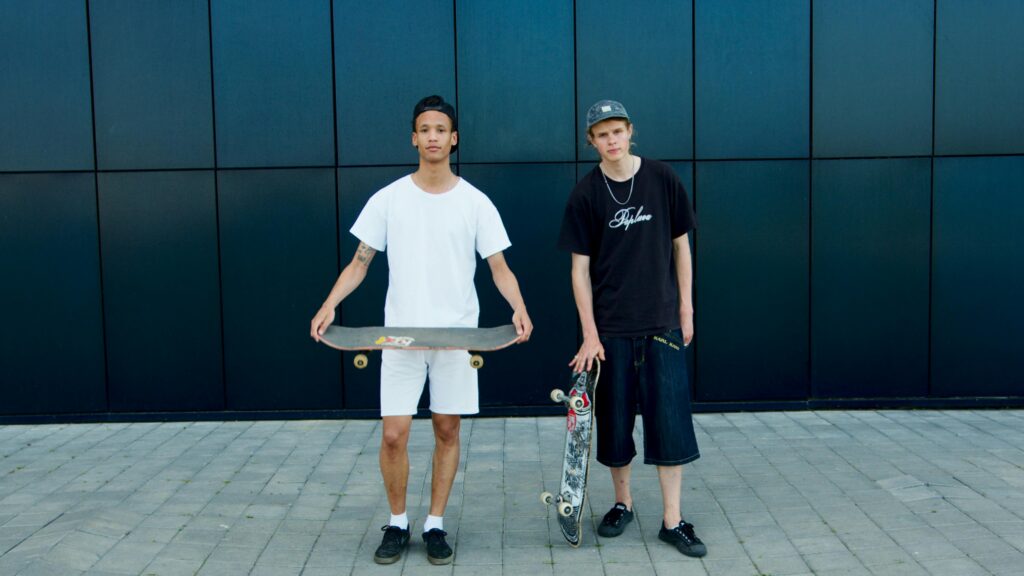 Two skaters standing outdoors holding skateboards, showcasing a casual and urban vibe.