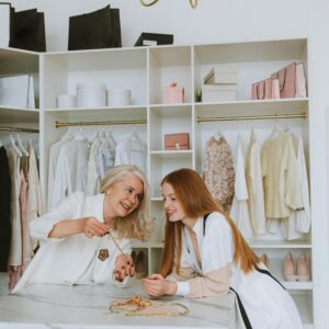 Two women laughing and selecting jewelry in a fashionable boutique setting.